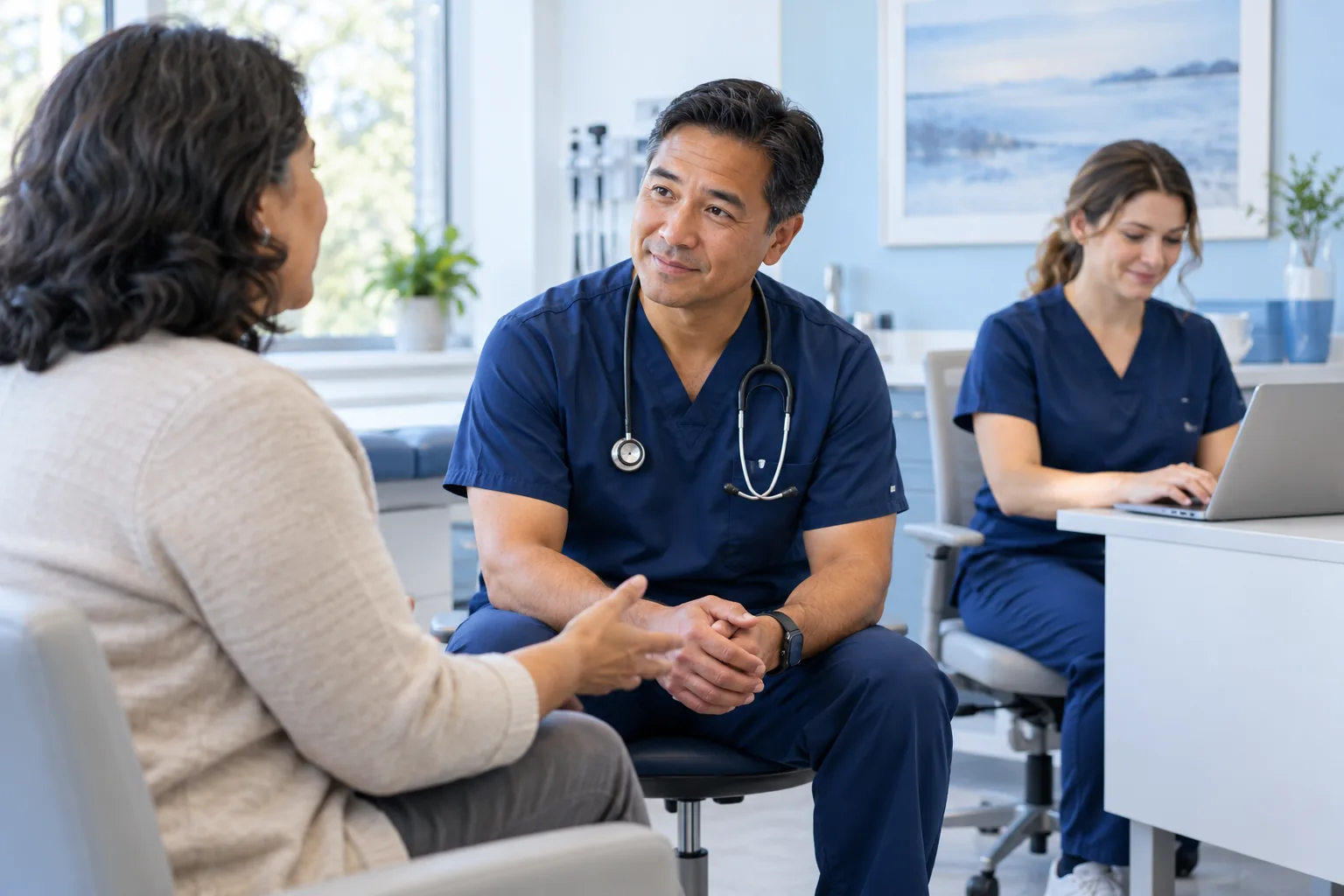 Physician listening to a patient while a medical scribe documents the visit